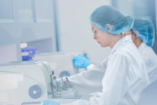 Professional histology technician cutting tissue section with microtome machine. Female scientist in safety gear preparing biopsy sample slide in sterile laboratory.