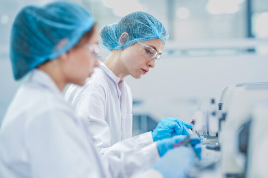 histology technician cutting tissue section with rotary microtome. Female scientist processing paraffin biopsy block in lab. Doctor in protective gear using microtome machine to analyze tissue sample.