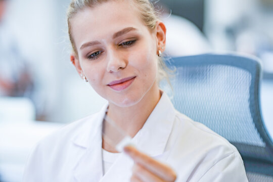 Professional histology technician cutting tissue section with rotary microtome. Female scientist in safety gear processing paraffin biopsy block in lab room.