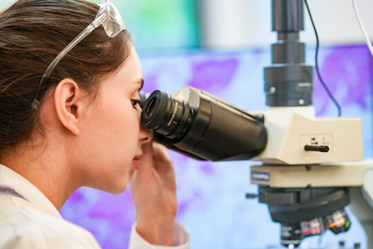 Medical pathologist adjusting microscope eyepiece for cancer diagnosis. Female scientist analyzing tissue biopsy sample in sterile hospital laboratory facility.