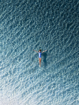 Aerial view of a woman floating in the crystal clear turquoise waters of Eagle Bay Beach with sunlight reflecting on the sandy seabed Naturaliste, Western Australia, Australia.