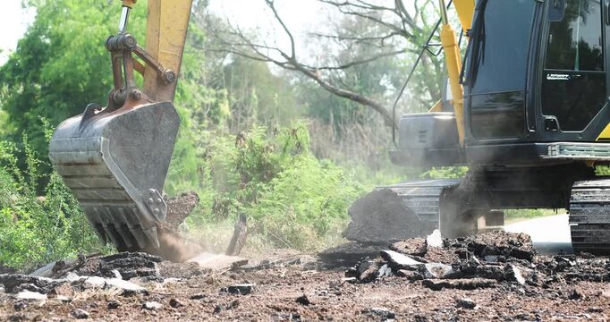 Excavator Digging Up Road Surface, Road construction and demolition, Excavator bucket digging, lifting broken asphalt and concrete debris, Excavator loading broken concrete at construction site