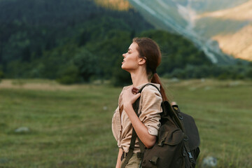 Obraz premium A woman with a backpack stands in a wide meadow, gazing upward as breeze lifts her hair. The scene conveys adventure, calm, and a strong connection with nature.