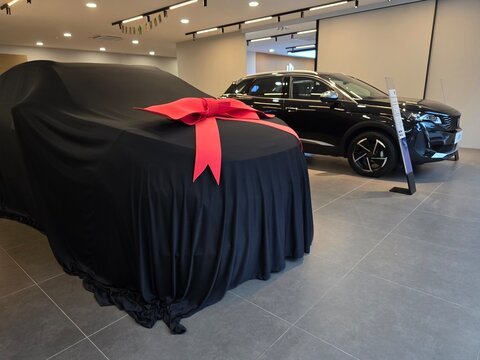 Penang, Malaysia - Apr 07, 2026: A black Peugeot 3008 SUV on display in a modern dealership next to a new vehicle covered in a black cloth with a large red gift ribbon, ready for a customer delivery.