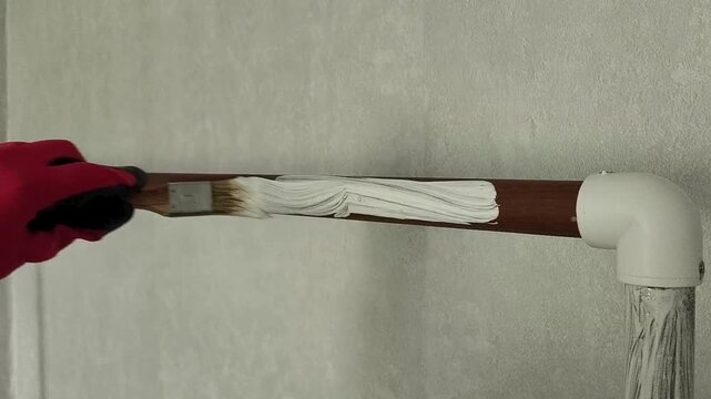 A painter's hand in a red glove holds a brush and paints a wooden board with white paint. Repainting furniture
