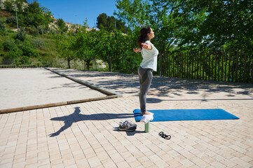 Naklejka premium Woman Doing Yoga Outdoors on Mat Stretching Arms for Balance and Fitness in Sunny Park