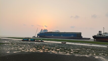 Cargo ships anchored at low tide on muddy shore during golden hour sunset, maritime scene © Abdur
