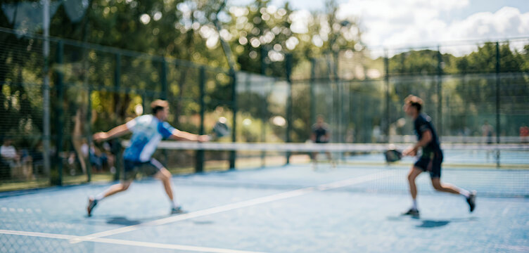 Abstract blurred tennis scene with multiple players in motion on a sunny court, offering a bright and energetic backdrop that conveys exercise, competition, and leisure activity.
