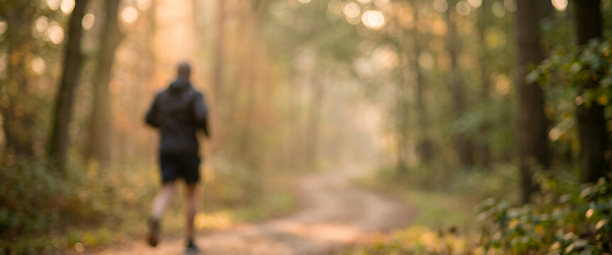 Blurred figure jogging along a forest path surrounded by golden sunlight and autumn foliage creates a warm and peaceful outdoor scene ideal for fitness and nature themes.