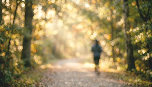 Motion blurred jogger travels down a leaf covered trail with warm golden tones and dreamy light, representing health, activity, and connection with nature.