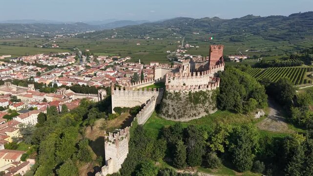 Cinematic drone footage of the Scaliger Castle in Soave, Verona. High angle view showing the ancient walls, fortification, and rural landscape of northern Italy.