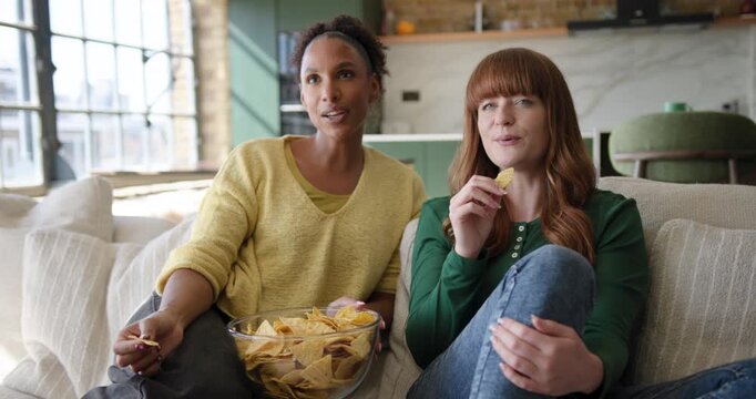 Female Friends at Home on Sofa Watching Movie and eating Crisps