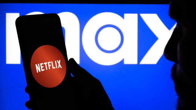 Person holding a smartphone with the netflix logo on the screen in front of a large imax logo on a blue background