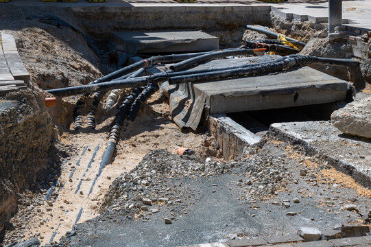 Deep excavation in an urban area showing various service pipes and cables. Infrastructure renovation project involving water, gas, or electrical network upgrades under the street