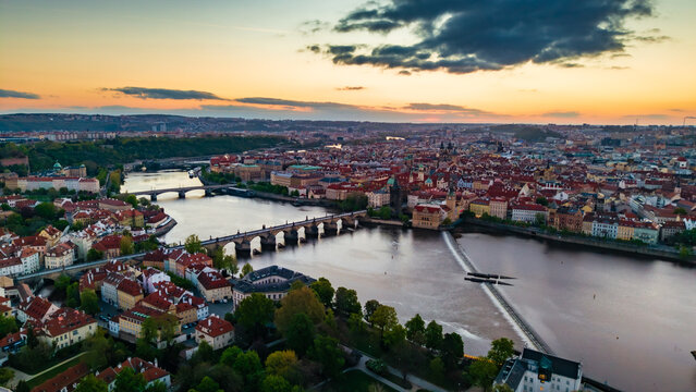 Aerial view of Charles Bridge spanning the Vltava River with historic rooftops and the city skyline under a sunset sky in Prague, Prague, Czechia.