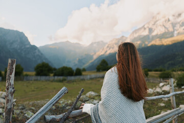 Woman with long hair in a knit sweater stands beside a wooden fence gazing at distant mountains, serene outdoor lifestyle scene, nature and wide open space. © SHOTPRIME STUDIO