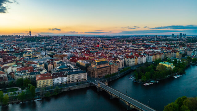 Aerial view of the National Theatre and the Vltava river with the historic city skyline under a sunset sky in Prague, Prague, Czechia.