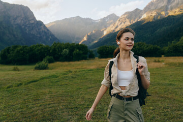 Naklejka premium Cheerful woman outdoors, walking through a sunlit meadow with mountains in the distance, casual hiking gear, backpack, relaxed expression, natural colors, fresh breeze, serene mood