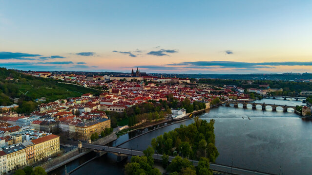 Aerial view of Prague Castle and Charles Bridge over the Vltava River with historic red rooftops and lush greenery at sunset in Prague, Prague, Czechia.