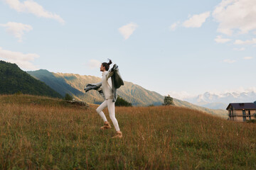 Naklejka premium Young woman with backpack hikes across a grassy field toward distant mountains, radiating carefree adventure and energy in an open landscape at golden hour with soft breeze.
