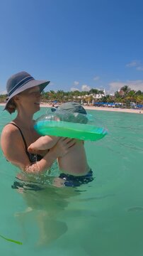 Mother swimming in the sea with her six month old baby boy wearing a floating neck ring. Slowmotion video.