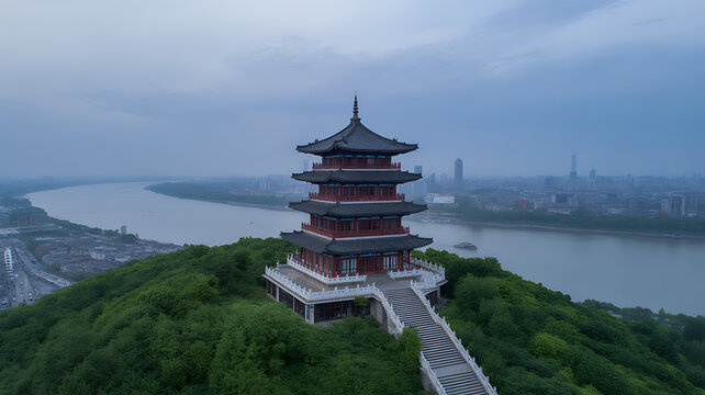 An aerial view of a traditional pagoda standing on a green hill overlooking the river and cityscape in Jiujiang China during a cloudy day
