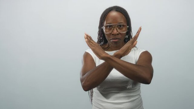 Young african american woman crosses forearms into an x gesture across chest while wearing glasses and white top in a studio; rejection boundaries.