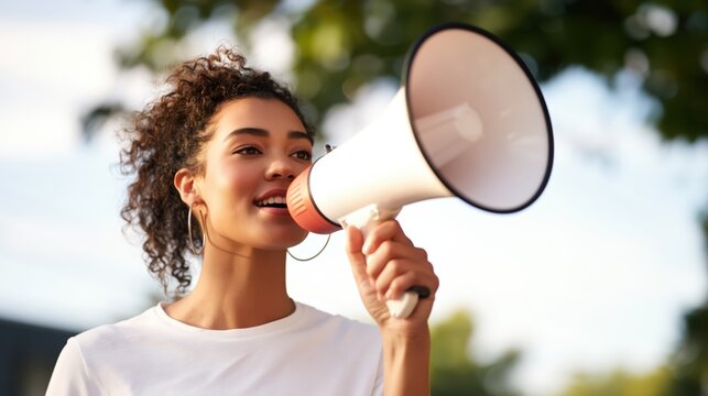 Smiling young woman speaking into a megaphone outdoors in natural light.