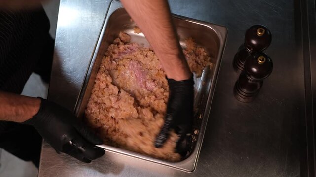 Chef in black rubber gloves mixing minced meat before cooking in professional restaurant kitchen top view close-up of hands

