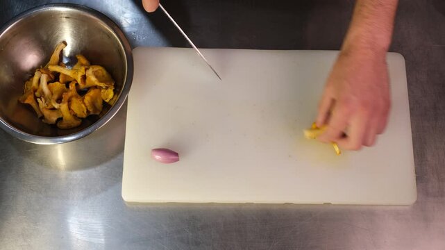 Chef in restaurant slicing chanterelle mushrooms into pieces on cutting board before cooking close-up of hands top view


