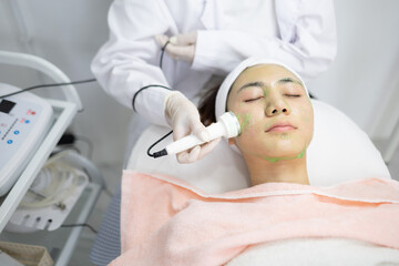 Naklejka premium Woman relaxes during facial treatment. Professional uses device gently on her face. Her eyes are closed, face calm and peaceful. Clinic environment appears clean and modern. Ideal for beauty, skincare