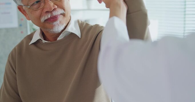 Young Asian female doctor examining senior man arm and shoulder at clinic. Physical therapy rehab, joint pain treatment, medical health care, professional physician support, muscle injury concept.