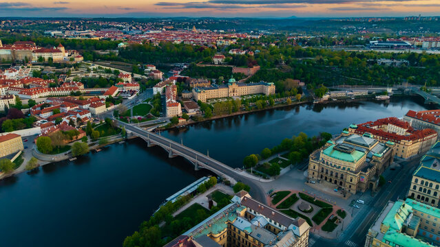 Aerial view of the Vltava River and Manes Bridge with the Rudolfinum and historic red rooftops under a sunset sky in Prague, Prague, Czechia.