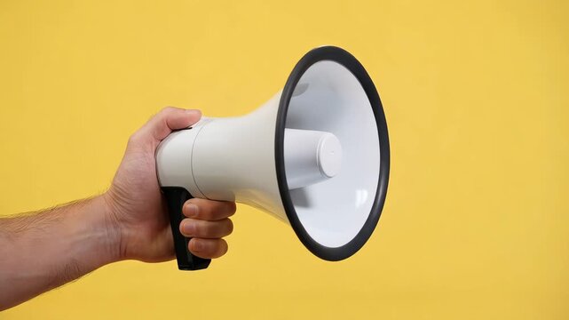 Hand holding a white megaphone against a bright yellow background for public announcement