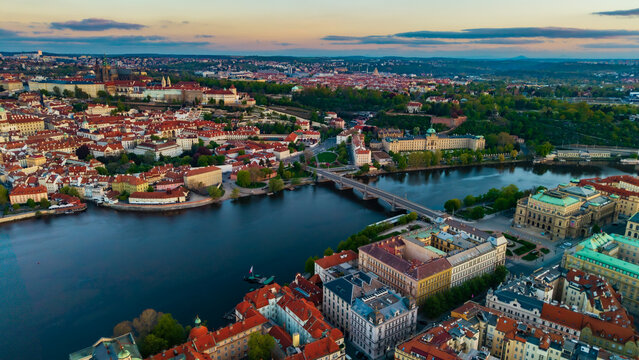 Aerial view of Prague Castle, the Vltava River, and historic red-roofed buildings under a soft sunset sky Prague, Prague, Czechia.