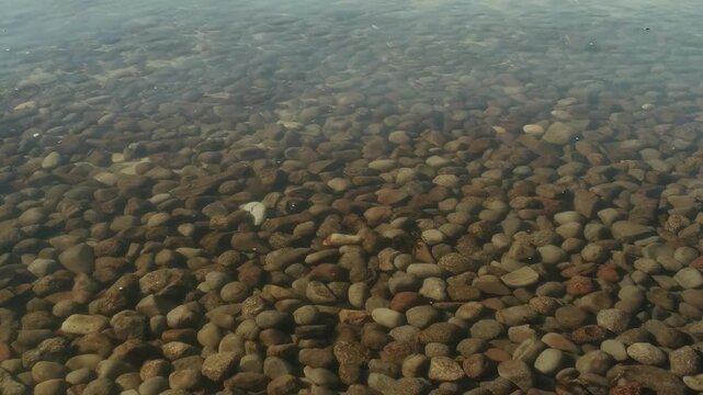 Clear water flowing over smooth river stones and pebbles on the seabed