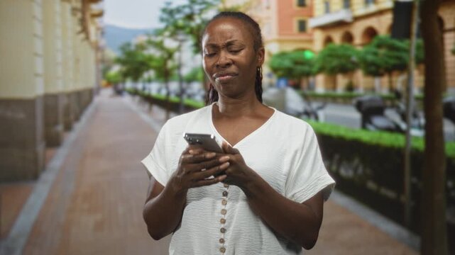 African american woman on a street holding smartphone to ear, gesturing with concerned face and later checking phone screen; frustration uncertainty.