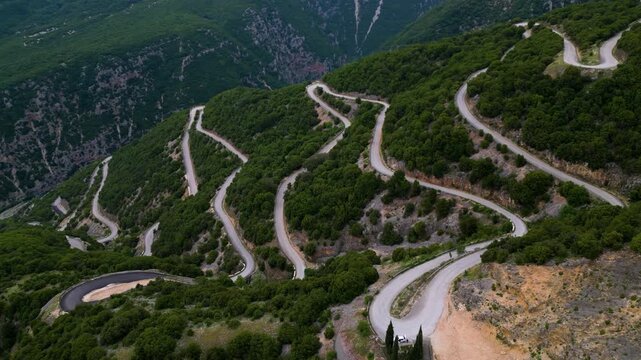 Drone footage of winding mountain roads in Tzoumerka Mountains, Northern Greece, in summer, aerial view of tight curves and switchbacks through lush green hills, remote landscape with no traffic