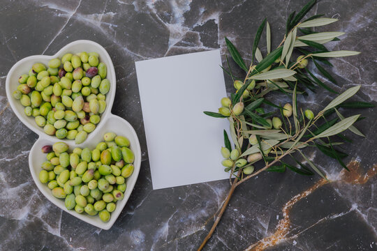 Healthy green olives in heart shaped white plate with tree branch, Mediterranean superfood rich in vitamins and minerals, blank paper for copy space