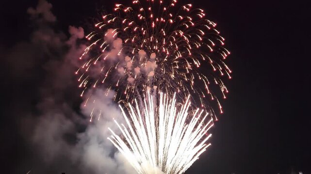 Red and white fireworks exploding in the dark night sky. Pyrotechnics display with smoke during a festive holiday celebration