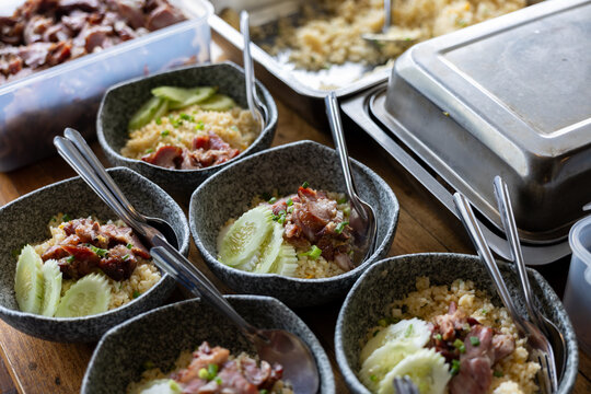Delicious savory rice bowls topped with roasted pork slices and fresh cucumber garnish arranged together on wooden table ready to be served for hearty and satisfying casual dining experience