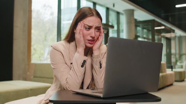 Caucasian young businesswoman girl using laptop notebook typing browsing, loses receive lottery results, bad news loss, fail, computer virus error in modern office lobby. Lady sitting in hotel hall