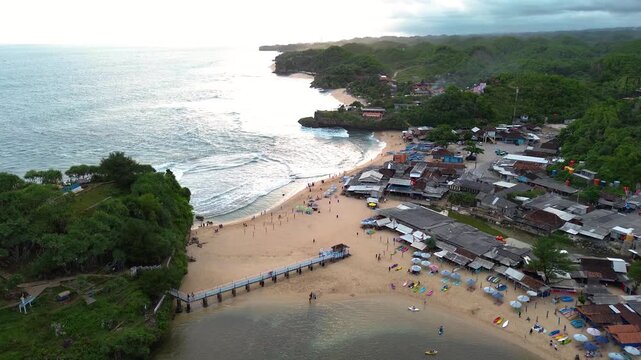 Aerial drone view of Drini Beach in Yogyakarta, Indonesia. Scenic tropical coastline with white sandy beach, clear turquoise water, small offshore island, and gentle ocean waves.