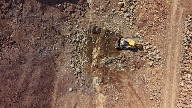 A large bulldozer works on rocky ground at a construction site. The machine digs into the earth while workers stand nearby, observing the progress in a developing area.