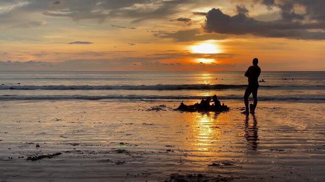 Golden sunset over the ocean with silhouettes of an adult and children building a sandcastle on wet sand. Family vacation moments, togetherness, and a relaxed beach lifestyle in a tropical destination