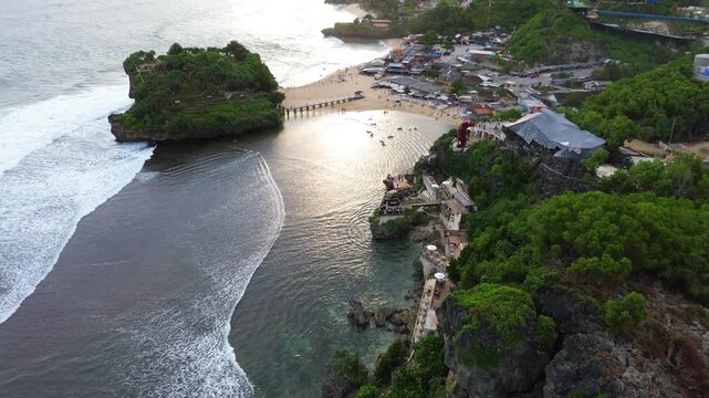 Aerial drone view of Drini Beach in Yogyakarta, Indonesia. Scenic tropical coastline with white sandy beach, clear turquoise water, small offshore island, and gentle ocean waves.