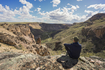 Fototapeta premium Wide angle view of man sitting on rock looking at epic valley of Pinturas River Canyon. Parque Patagonia, Argentina