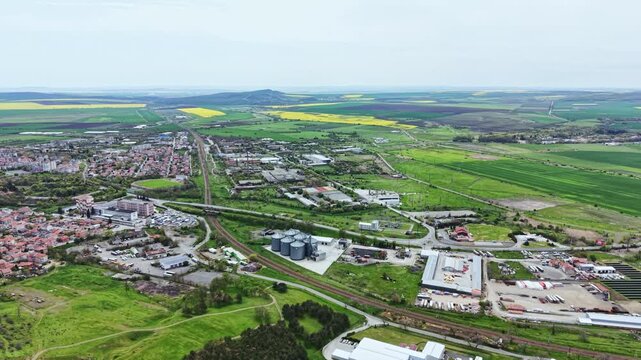 A mix of rural and urban areas with fields, roads, buildings, and storage tanks. The view captures the layout and structure of the land in daylight.