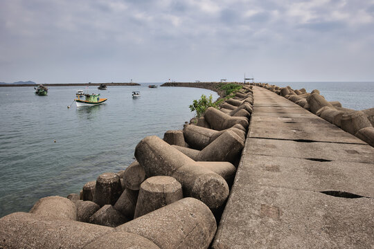 Manmade breakwater protecting coastline with boats under dramatic sky in Marang, Terengganu