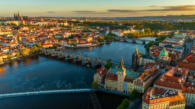 Aerial view of Charles Bridge crossing the Vltava River with Prague Castle and the historic Old Town rooftops under a warm sunset glow in Prague, Prague, Czechia.